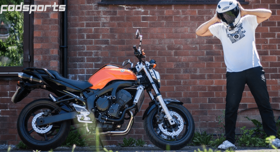 A motorcycle rider stands on the side of the road covering his ears