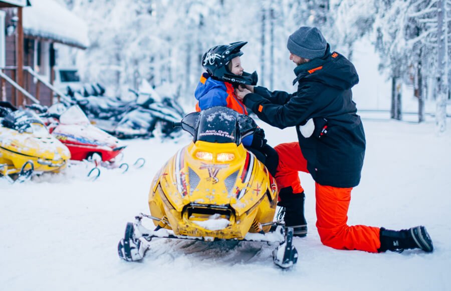 a father is helping his child organize snowmobiling equipment - Snowmobile Age Requirements