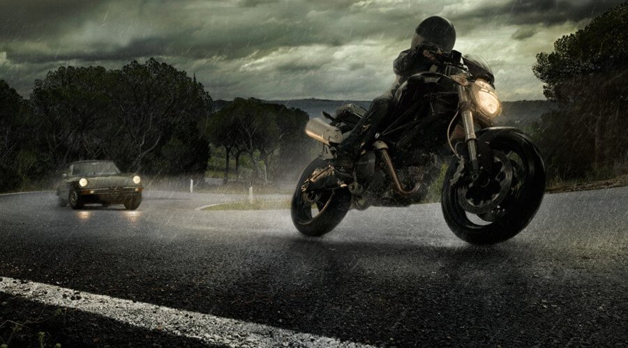 a motorcycle overtakes a car in the rain