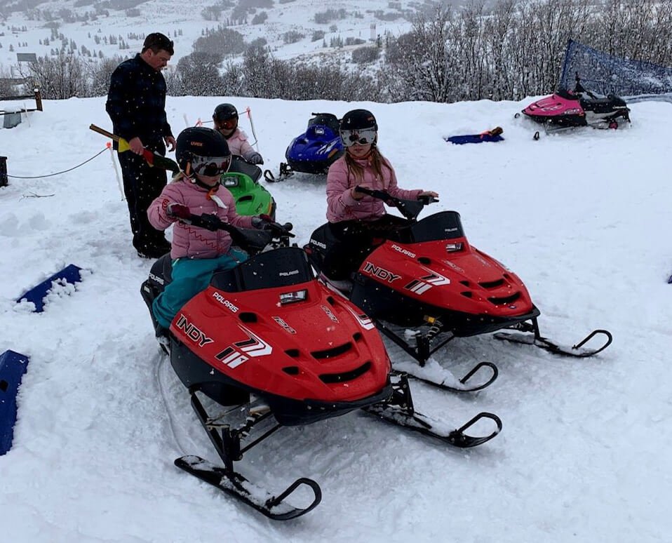 children are riding snowmobiles under adult supervision