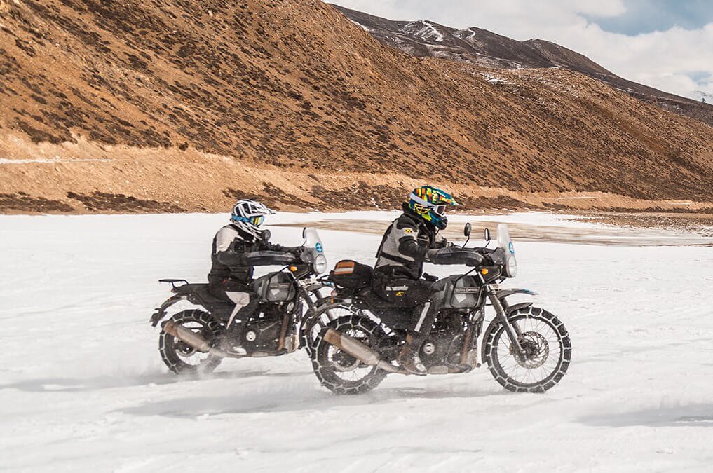 two men ride motorcycles in the winter snow