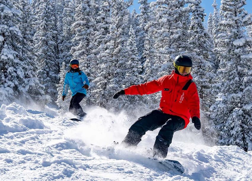 two snowboarders is snowboarding in the forest